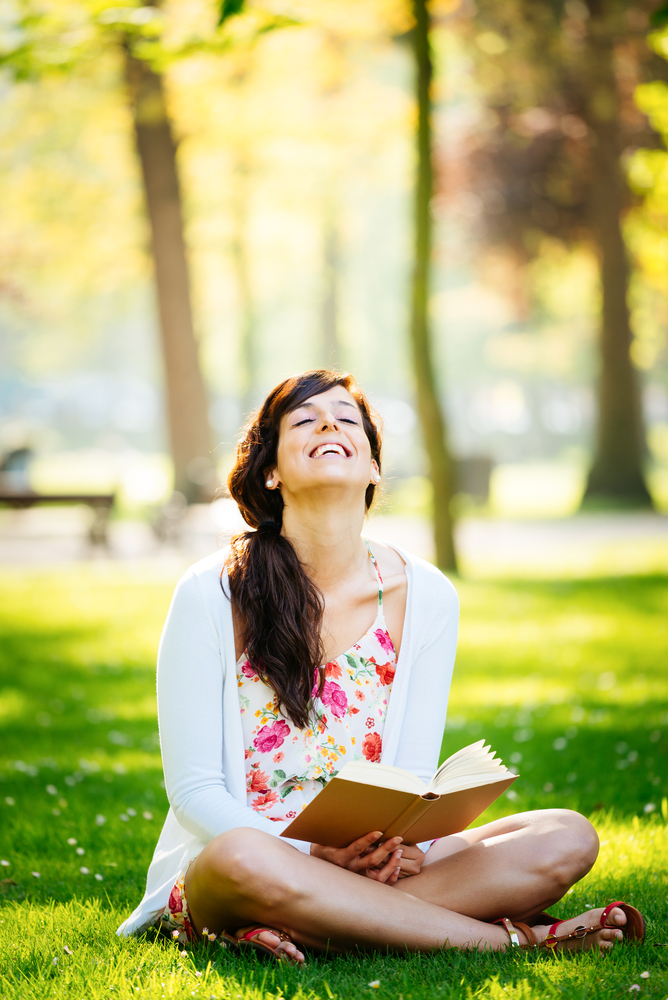 Joyful woman reading fun book sitting on grass in park